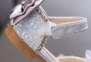 Dettaglio ravvicinato di sandalo glitter argento per bambina con fiocco in raso e cristalli