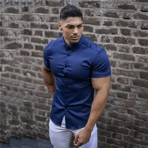Detail of navy muscle fit short-sleeved shirt on model with brick wall backdrop.