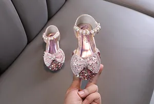 Close-up of pink girl's princess shoes featuring a glittery rhinestone bow and pearls