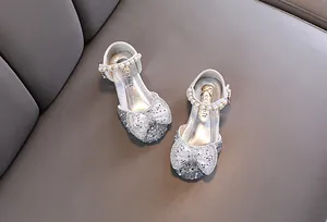 Detailed view of silver girls' princess shoes with rhinestones, pearls, and a large bow.