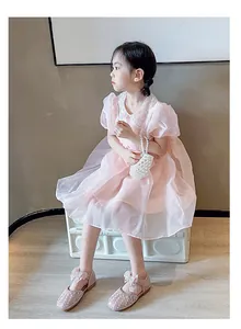 Elegantes Mädchen im rosa Tüllkleid mit Schleifen-Perlen-Prinzessinenschuhen im gemütlichen Raum.