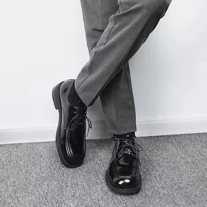 Nahaufnahme der glänzenden schwarzen Herrenschuhe mit eckiger Kappe und grauer Hose