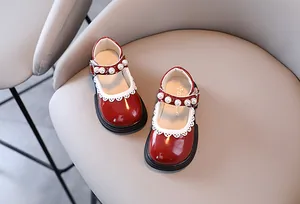 Close-up of red patent leather girls' shoes with pearl strap and lace trim