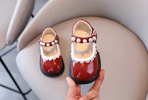 Close-up detail of red patent leather girl's Mary Jane shoes with pearls and lace trim.