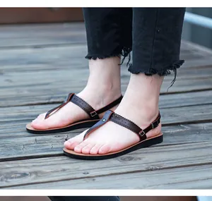 Close-up of brown PU leather thong sandals with laser-cut straps on a wooden deck