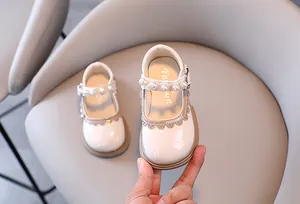 Close-up of girls' cream patent leather princess shoes with pearl strap and scalloped trim