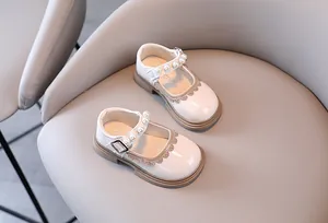Close-up of white patent leather girls' shoes with pearl straps and scalloped trim details
