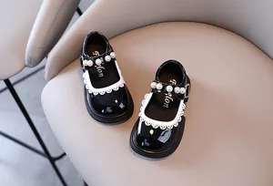 Top-down view of black patent leather girls' shoes with pearl strap and lace trim.