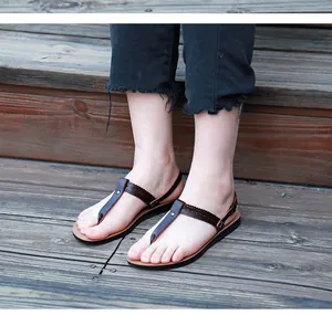 Detail view of brown T-strap PU leather sandals being worn on outdoor wooden steps