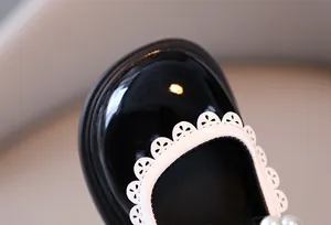 Macro view of girls' black patent leather shoes with white scalloped lace trim and pearls