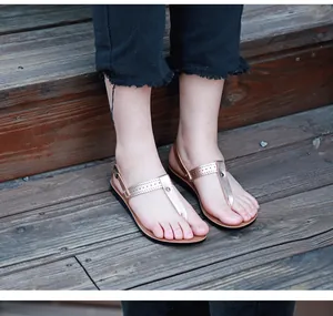 Close-up of rose gold flat sandals with hollow-out T-strap pattern worn on wooden stairs