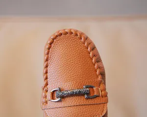 Close-up of brown pebbled leather boy's loafers with engraved metal buckle detail