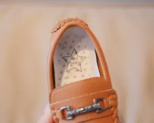 Close-up of brown boy's loafer showing the M.G BABY star logo insole and metal buckle.