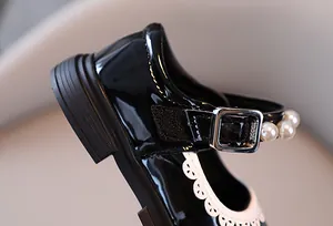 Detailed view of girls black patent leather Mary Jane shoe with elegant pearl strap and buckle