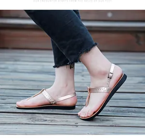 Detailed view of fashionable rose gold T-strap flat sandals worn on wooden deck