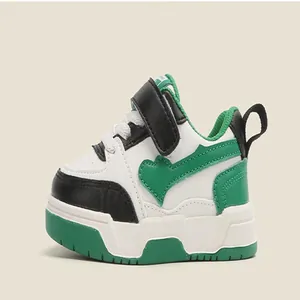 Side view of children's green and white sports shoes with heart detail and soft sole.