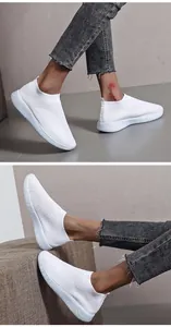 Detail view of white breathable fly-knit slip-on sneakers worn by a model in casual jeans