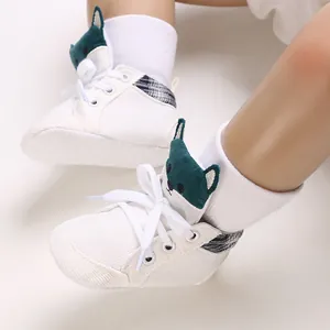 Primer plano de zapatos de gateo blancos para bebé con un bordado de perro verde