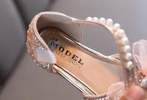 Close-up detail of pink children's princess shoe featuring pearl strap and rhinestone decor
