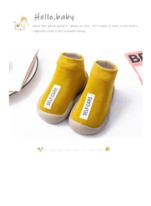 Close-up detail of yellow soft-sole baby sock shoes featuring a white Self-Care label.