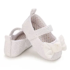 Détail de chaussures de princesse blanches pour bébé avec broderie en dentelle et nœud.