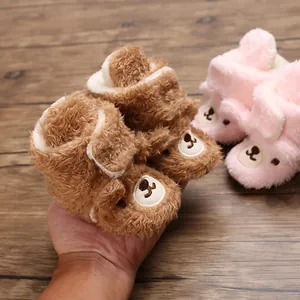 Nahaufnahme von weichen Plüsch-Babyschuhen mit süßem Bärendesign in der Hand