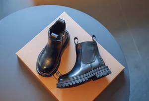 Gros plan sur des bottines Chelsea noires pour enfants posées sur une boîte en carton brun