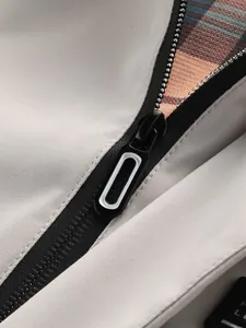 Detailopname van de rits en de klassieke geruite voering van een beige jas.