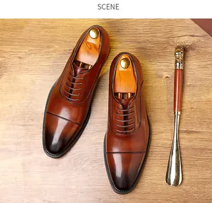 Polished brown leather cap-toe Oxford shoes with wooden shoe trees on floor