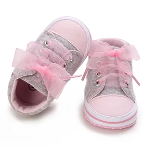 Close-up of pink and grey polka dot baby shoes with decorative mesh bows and soft soles.