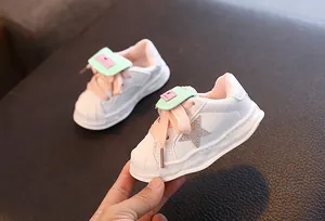 Close-up of white leather children's star sneakers with pink laces and mint green accents.