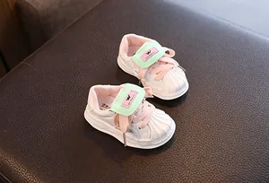 Close-up view of children's white shell-toe sneakers with pink laces and green straps