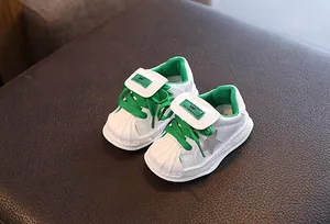 Children's white leather shell-toe sneakers with green laces and star detail.