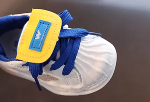Macro detail view of a white toddler sneaker with blue laces and classic shell toe design