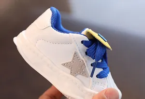 Macro detail of white children's leather sneakers featuring blue laces and a grey star.