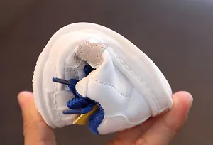 Detailed view of flexible white shell-toe sneakers for kids with blue laces and stars
