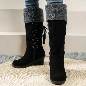 Close-up view of black tall wedge snow boots with faux fur cuff and back tassels