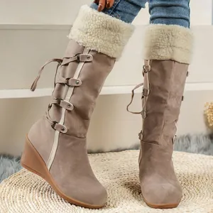 Detail of suede knee-high wedge boots with faux shearling cuff and side-lace decoration.