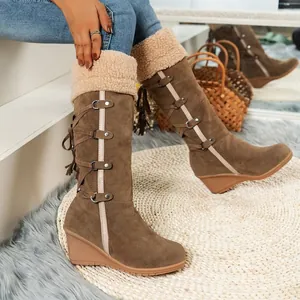Detailed side view of brown high-top snow boots with fringe tassels and wedge heels