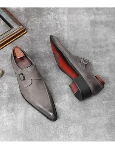 Detailed view of grey suede monk strap dress shoes featuring a pointed toe and red sole.