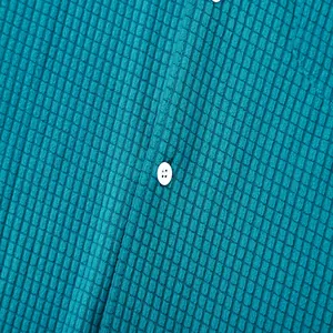 Macro detail of the waffle texture fabric and white button on a teal blue men's shirt.