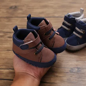 Main tenant des chaussures de marche bébé en toile marron et bleu à semelles souples.