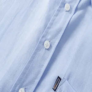 Macro detail of a light blue Oxford shirt showing white buttons and a pocket label.