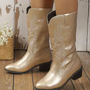 Gros plan de bottes de cowboy dorées à mi-mollet avec des broderies blanches raffinées