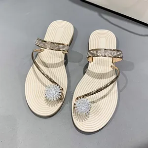 Close-up detail of elegant beige flat sandals with rhinestone flower and gold straps
