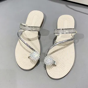 Detailed view of silver toe-loop flat sandals with sparkling rhinestone sunflower accents.