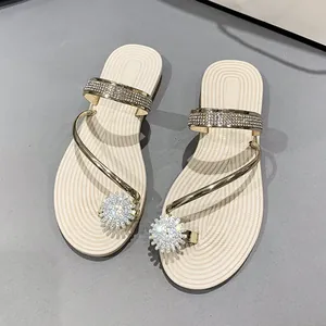 Detailed view of beige flat sandals with gold straps and sparkling rhinestone flower.