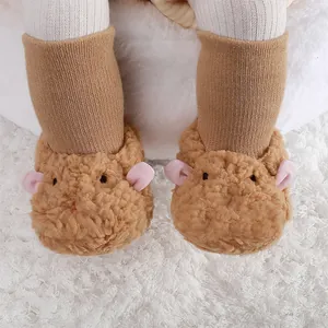 Vue détaillée de chaussons en peluche pour bébé avec des oreilles roses sur un tapis blanc