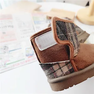 Close-up of brown children's snow boot featuring plaid trim and a velcro strap.