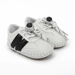 Vista detallada de zapatos blancos para bebé con costuras y toques negros sobre fondo blanco